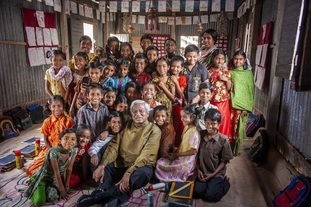 Sir Fazle Hasan Abed seated with children inside a BRAC school classroom.